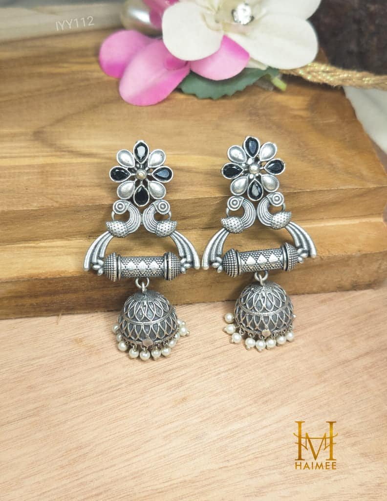 silver oxidized jhumka of brass with pearl motifs and black stones placed on wooden surface